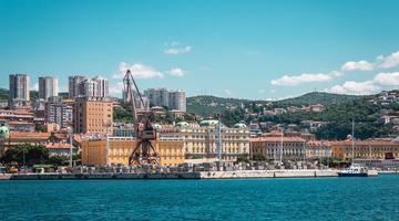 a picture of the Waterfront in Rimini. A crane is visible in front of a promenade with buildings from the early 20th or 19th century with a yellow taint.
