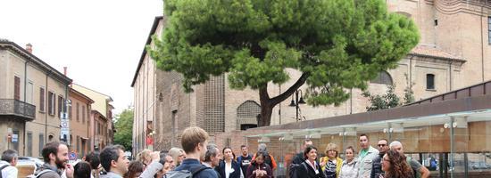Particiants on study visit A group of people standing around listening to a presenter outside. The background includes some buildings that look like heritage buildings and a beautiful tree.