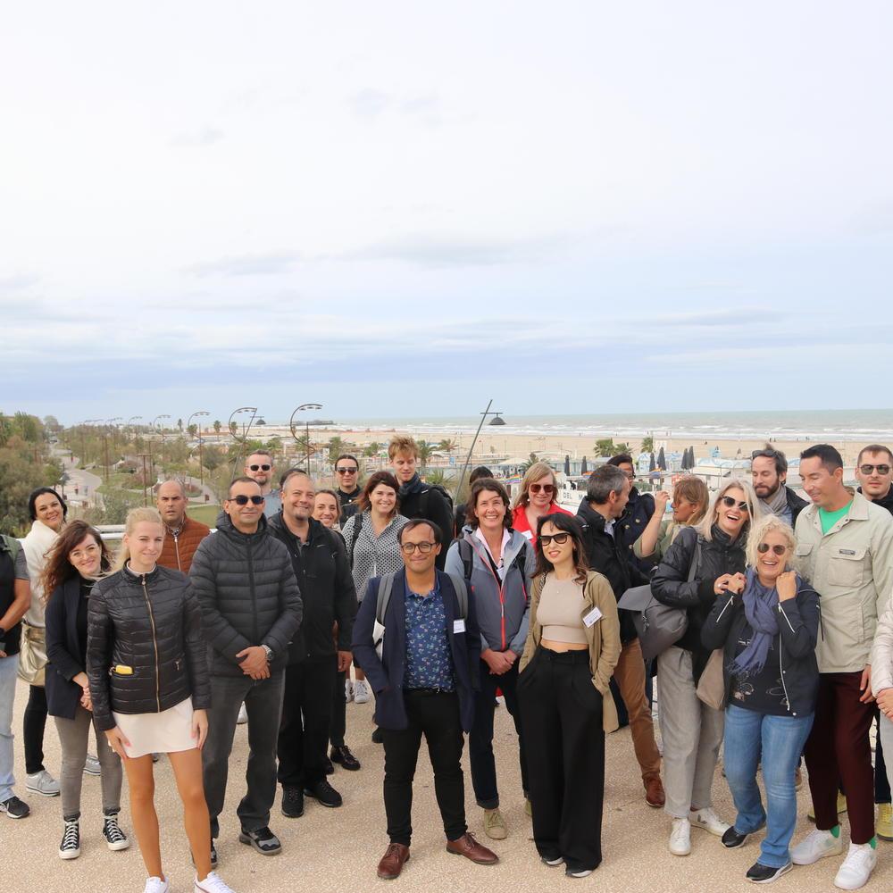 A picture of the full group of participants at the study tour, with the beach, water and a stretch of the waterfront park Parco del Mare in the background