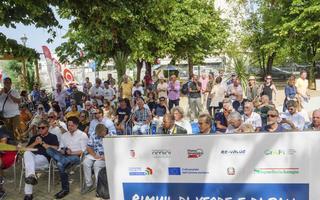 A picture of a large group of people sitting down outside listening to a presentation. In the foreground is a banner including Re-Values logo and a statement to many of the projects being funded by European funds