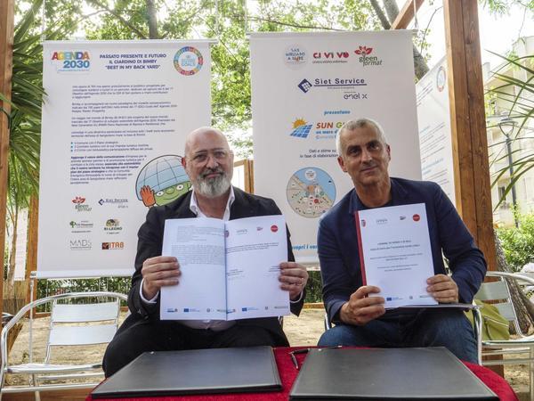 The President of the Emilia-Romagna Region, Mr. Stefano Bonaccini (left) and the Mayor of Rimini, Mr. Jamil Sadegholvaad A picture of two gentlemen presenting the Rimini plans. They sit in front of two large banners showing documents to the camera